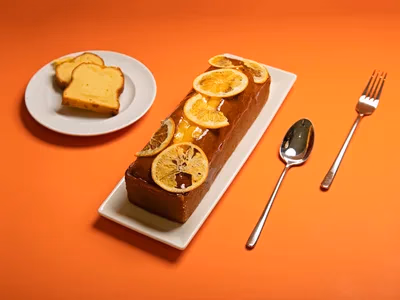 Bolo de laranja fit fatiado em prato branco com rodela de laranja fresca por cima