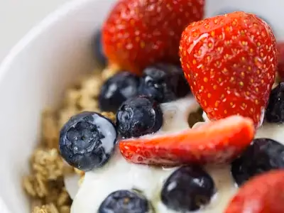 Bowl de iogurte grego com granola dourada e frutas frescas coloridas