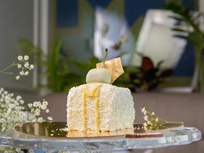 Fatia de bolo de coco gelado com base crocante e creme branco em prato com coco ralado