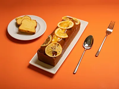 Bolo de laranja fit fatiado em prato branco com rodela de laranja fresca por cima