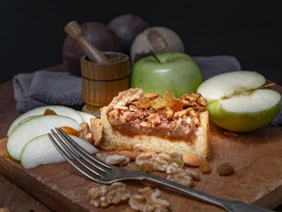 Fatia de bolo de maca com canela e nozes em prato de madeira com maca fresca ao lado