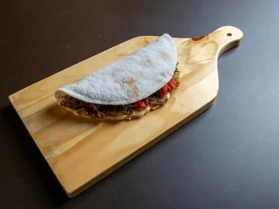 Tapioca dobrada ao meio com recheio de frango desfiado ao fundo verde