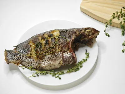 Filé de tilápia dourado assado com ervas verdes e fatias de limão